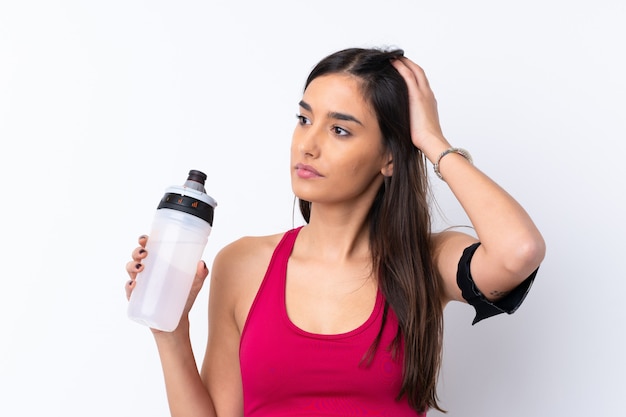 Jeune femme brune sport sur mur blanc isolé avec bouteille d'eau de sport