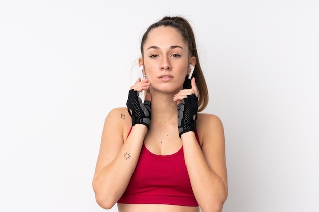 Jeune femme brune sport sur mur blanc isolé écouter de la musique et regarder vers l'avant