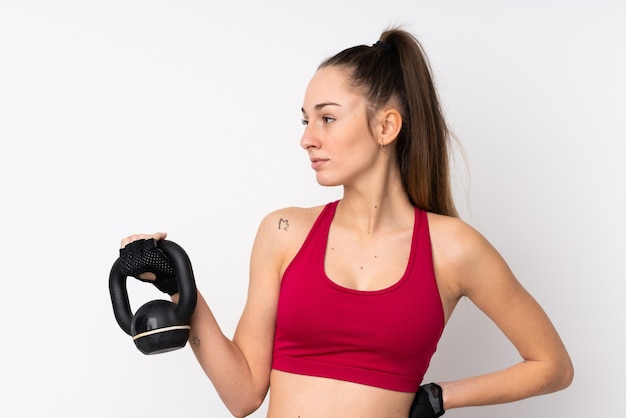 Jeune femme brune sport sur mur blanc isolé faisant de l'haltérophilie avec kettlebell