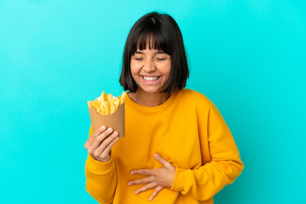 Jeune femme brune tenant des chips frites sur fond bleu isolé souriant beaucoup