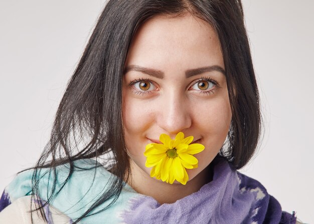 Jeune femme brune tenant une fleur jaune dans sa bouche