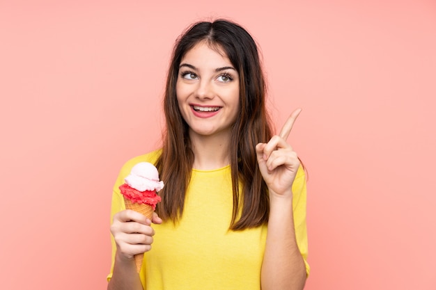 Jeune femme brune tenant une glace au cornet sur un mur rose isolé dans l'intention de réaliser la solution tout en levant un doigt