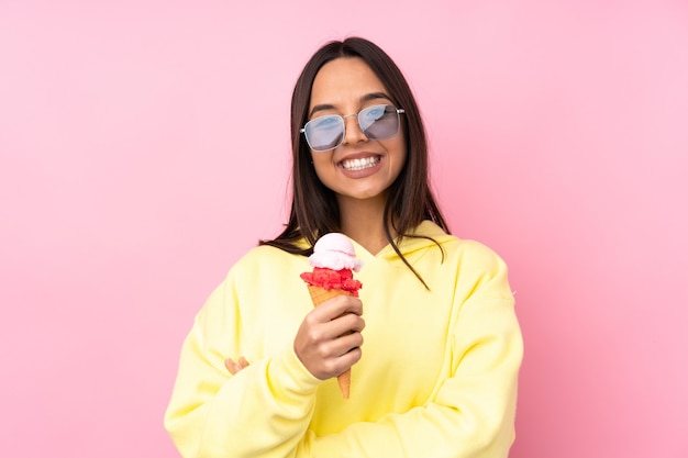 Jeune femme brune tenant une glace au cornet sur rose isolé en levant tout en souriant