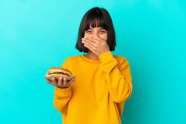 Jeune Femme Brune Tenant Un Hamburger Sur Fond Isolé Heureux Et Souriant Couvrant La Bouche Avec La Main