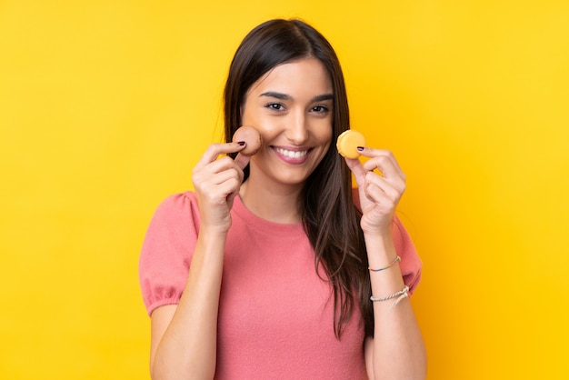 Jeune femme brune tenant des macarons français colorés et souriant