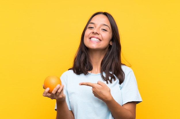 Jeune femme brune tenant une orange et en la pointant