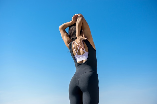 Jeune femme brune en tenue de sport faisant étirement ses jambes après l'entraînement sur le lac près de la journée. Mode de vie sain