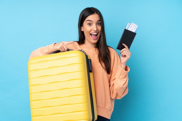 Jeune femme brune en vacances avec valise et passeport et surpris