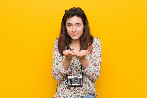 Jeune femme brune voyageur tenant quelque chose avec des paumes, offrant à la caméra.