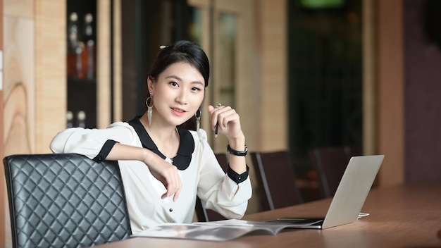 Une jeune femme de bureau est assise avec un ordinateur portable à la table de réunion.
