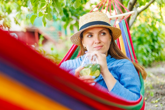 Une jeune femme buvant un cocktail alors qu'elle est allongée dans un hammock confortable dans un jardin vert