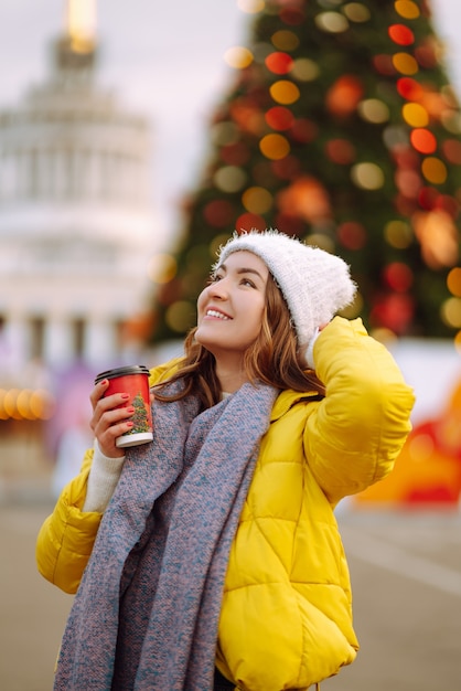 Jeune femme buvant du café chaud en marchant près de l'arbre du nouvel an.