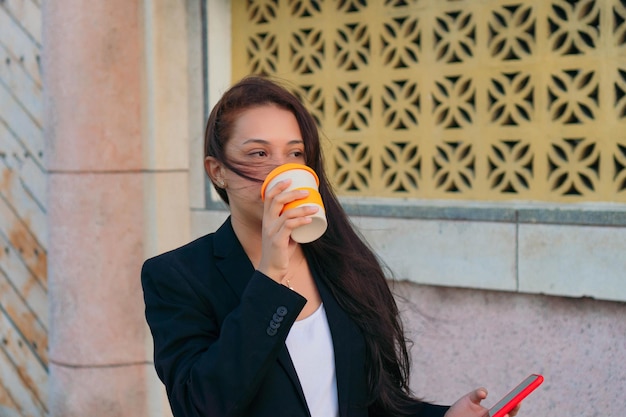 Jeune femme buvant du café et tenant un téléphone portable