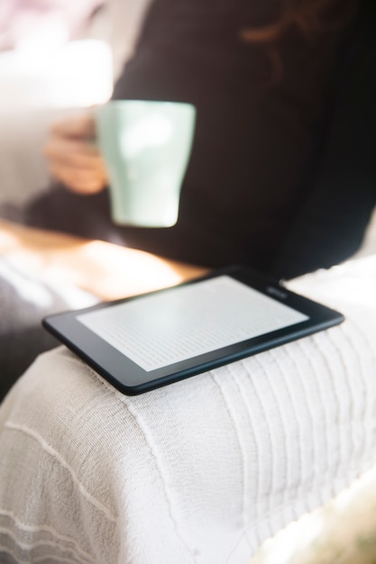 Jeune femme buvant du café et utilisant un lecteur d&#39;ebook