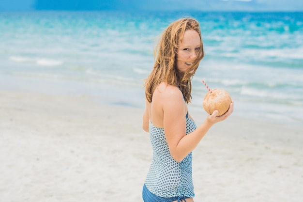 Jeune femme buvant du lait de coco sur la plage