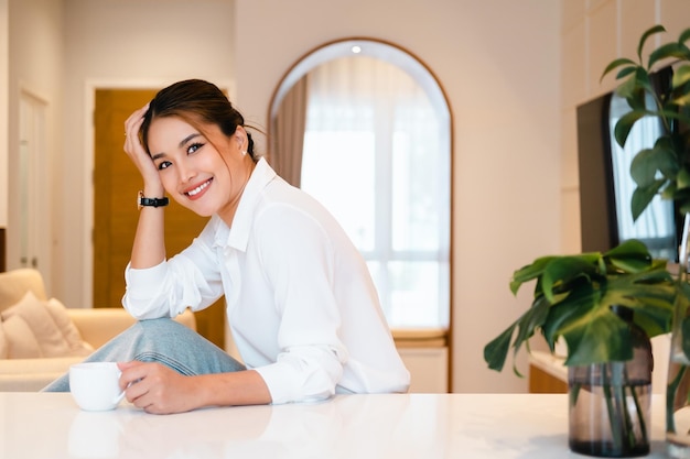 jeune femme buvant du thé ou du café dans sa cuisine tout en se préparant à aller travailler