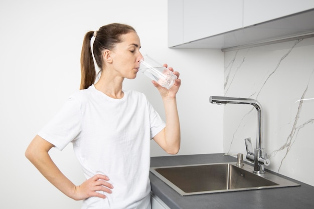 Jeune femme buvant de l'eau d'un verre dans la cuisine