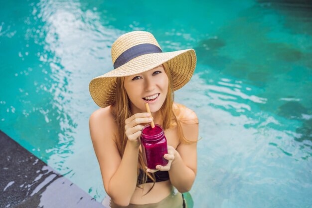 Jeune femme buvant des smoothies aux fruits du dragon sur le fond de la piscine Smoothie aux fruits concept d'alimentation saine Gros plan sur un smoothie détox aux fruits du dragon