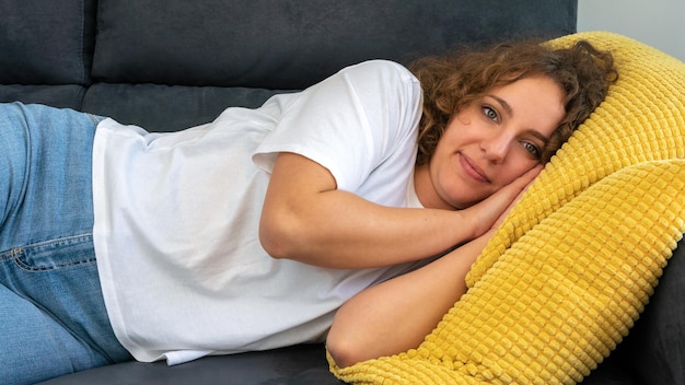 Jeune femme calme et sereine aux cheveux bouclés se reposant sur un canapé dans l'appartement confortable