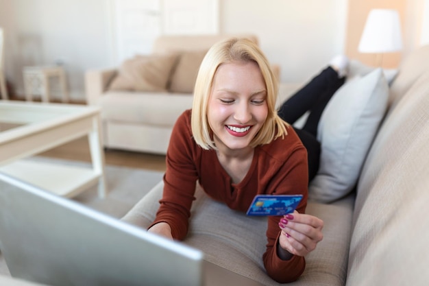 Jeune Femme Sur Le Canapé Achats En Ligne Avec Carte De Débit. Belle fille utilisant un ordinateur portable pour faire des achats en ligne à la maison