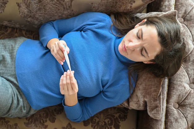 La jeune femme sur le canapé mesure la température