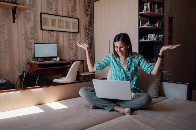 Jeune femme sur un canapé travaillant joyeusement sur un nouveau projet avec un ordinateur portable à la maison