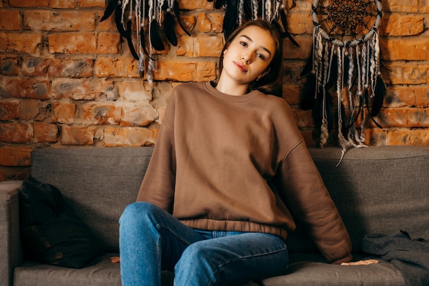 Photo jeune femme à capuche posant en studio sur l'espace de mur de brique