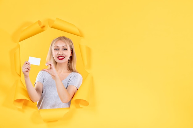 Jeune femme avec carte de crédit sur fond jaune shopping argent du visage