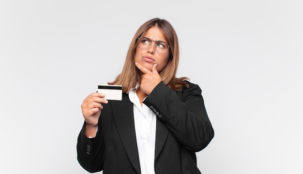 Jeune femme avec une carte de crédit pensant, se sentant dubitative et confuse, avec différentes options, se demandant quelle décision prendre