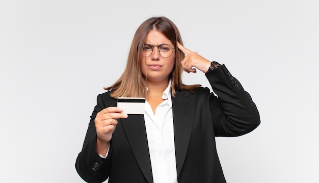 Jeune femme avec une carte de crédit se sentant confuse et perplexe, montrant que vous êtes fou, fou ou hors de votre esprit