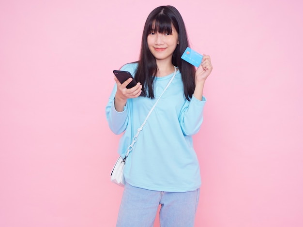 Jeune femme avec carte de crédit et smartphone sur mur rose. Shopping en ligne