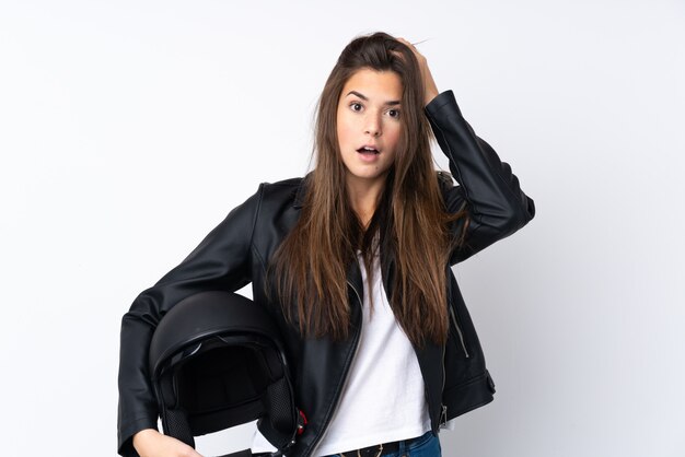 Jeune femme avec un casque de moto sur un mur blanc isolé avec une expression faciale surprise