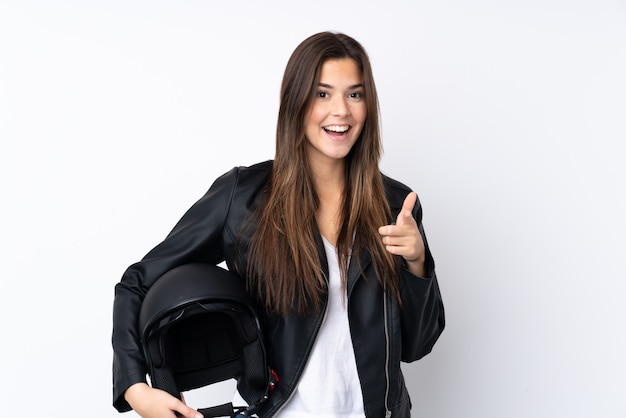 Jeune femme avec un casque de moto sur un mur blanc isolé pointe le doigt vers vous