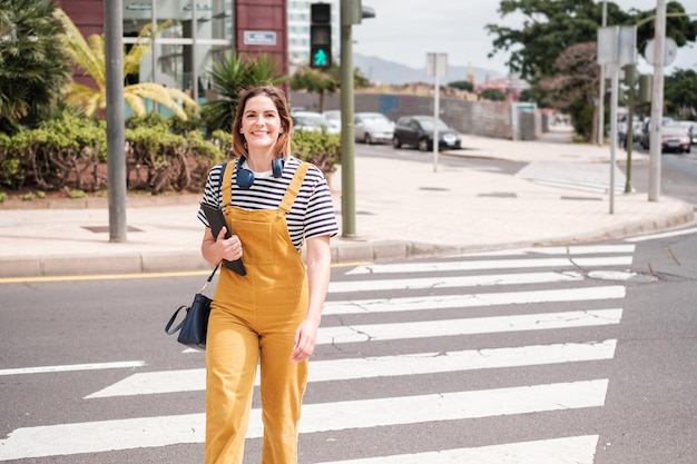 Jeune femme avec un casque sans fil traversant la rue au passage pour piétons Concept Lifestyle extérieur coucher de soleil