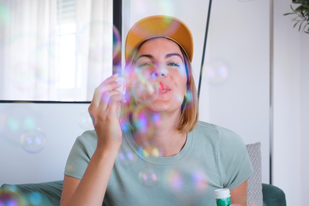 Jeune femme en casquette jetant des bulles de savon à l'intérieur de l'appartement Concept bonheur amusant nomade numérique