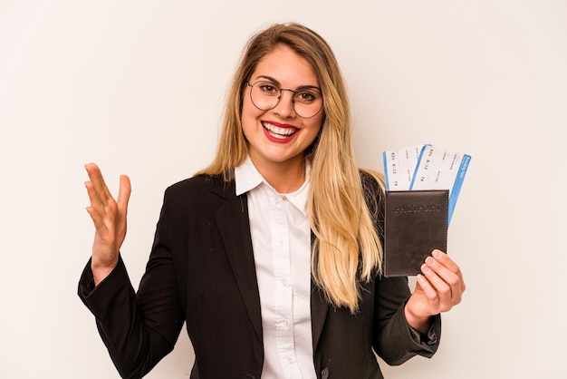 Jeune femme caucasienne d'affaires détenant un passeport isolé sur fond blanc recevant une agréable surprise excitée et levant les mains