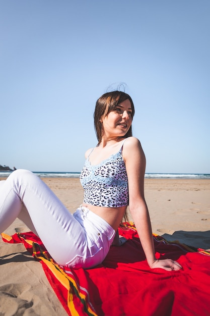 Jeune femme caucasienne assise sur une serviette à la plage