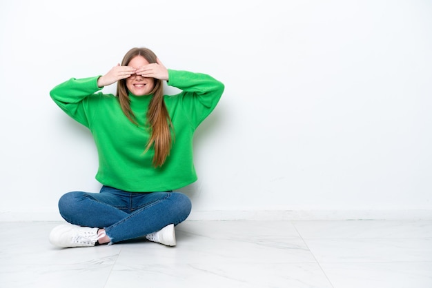 Jeune femme caucasienne assise sur le sol isolé sur fond blanc couvrant les yeux par les mains