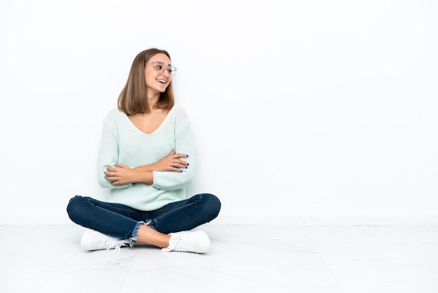 Jeune femme caucasienne assise sur le sol isolé sur fond blanc heureux et souriant