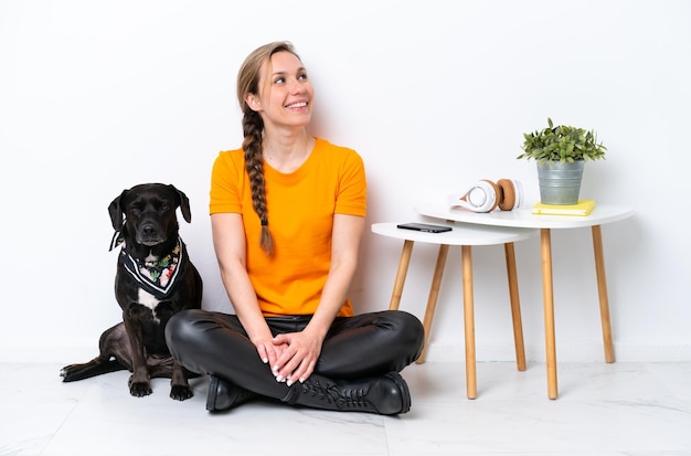 Jeune femme caucasienne assise sur le sol avec son chiot isolé sur fond blanc levant les yeux en souriant