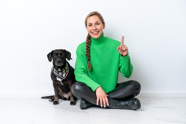 Jeune femme caucasienne assise sur le sol avec son chiot isolé sur fond blanc pointant vers le haut une excellente idée