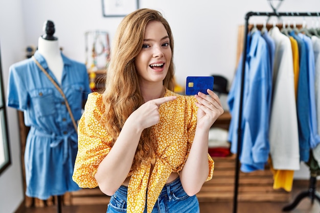 Jeune femme caucasienne au magasin de détail détenant une carte de crédit souriante heureuse pointant avec la main et le doigt