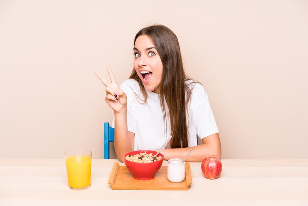 Jeune femme caucasienne ayant un petit déjeuner isolé joyeux et insouciant montrant un symbole de paix avec les doigts.