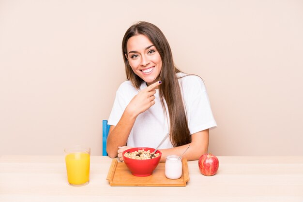 Jeune femme caucasienne ayant un petit déjeuner isolé souriant et pointant de côté, montrant quelque chose à l'espace vide.