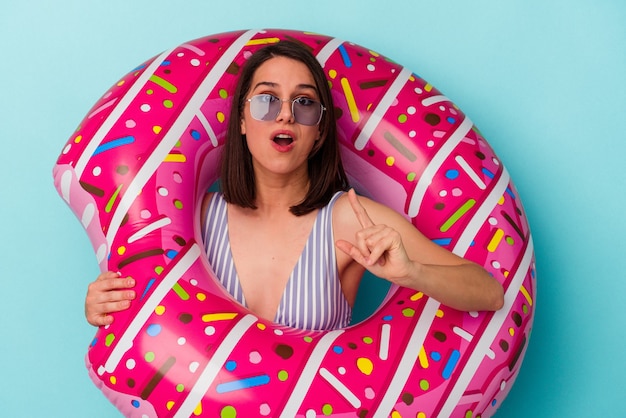 Jeune femme caucasienne avec beignet gonflable isolé sur fond bleu ayant une idée, concept d'inspiration.