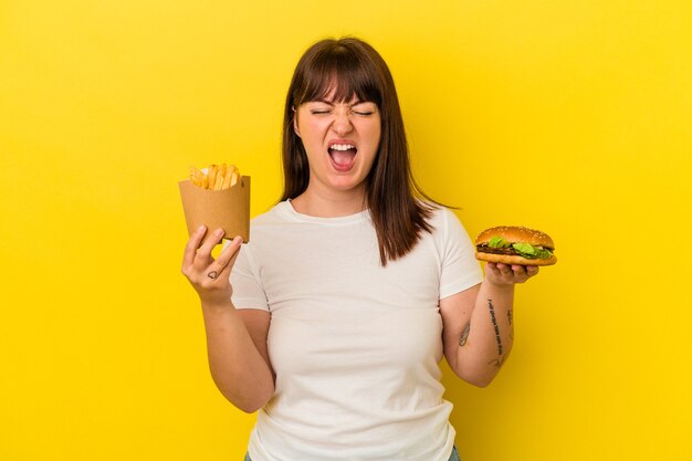 Jeune femme caucasienne bien roulée tenant un hamburger isolé sur fond jaune