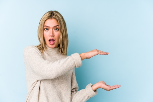 Jeune Femme Caucasienne Blonde Isolée Choquée Et étonnée Tenant Un Espace De Copie Entre Les Mains.