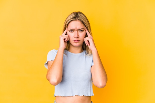 Jeune femme caucasienne blonde isolée sur un mur jaune concentré sur une tâche, gardant l'index pointant la tête.