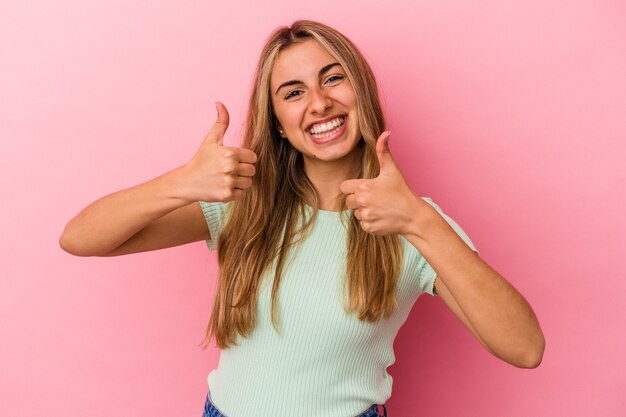 Jeune femme caucasienne blonde levant les deux pouces vers le haut, souriante et confiante.