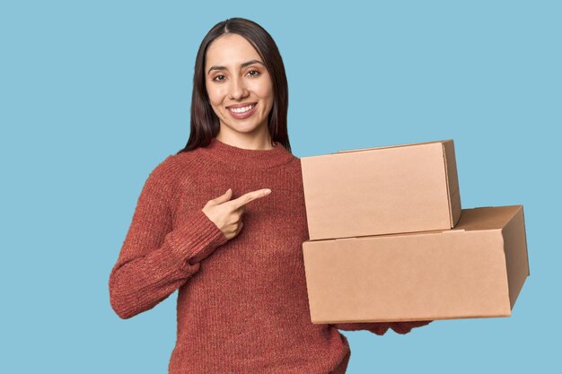 Une jeune femme caucasienne avec des boîtes en mouvement souriant et pointant du côté montrant quelque chose à l'espace vide